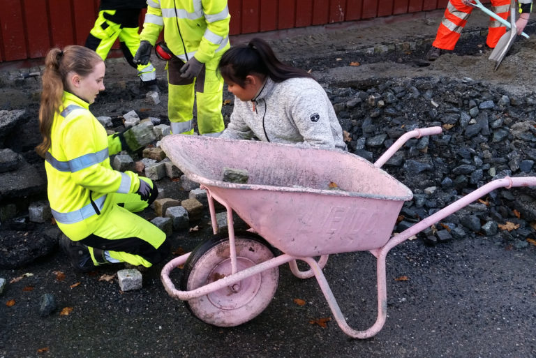 Kristin Olsnes Holsen (til venstre) hiver smågatestein i trillebåra.