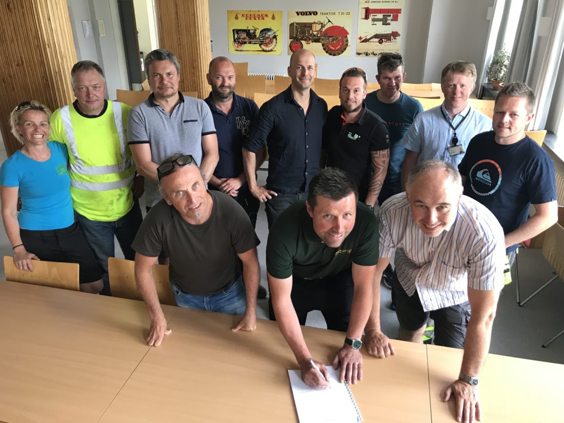 Tore Færevaag fra Os Hageservice AS signerer den nye samfunnskontrakten flankert av Geir Boge fra OKAB og rektor Magnus Vaktskjold fra Stend vgs. Bak ser vi de øvrige anleggsgartnermesterne som var til stede, samt representanter fra lærerstab og administrasjon ved Stend vgs. (Foto: OKAB).