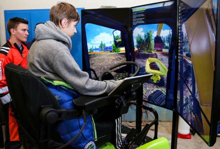 SIMULATOR: Viktor Schau (16), som går Vg1 bygg- og anleggsteknikk på Borg videregående skole, prøver anleggsmaskinsimulatoren. Ved siden av står Truls Johannesen (17), en av tre Vg2-elever fra Kalnes vgs. som var med for å bistå Vg1-elevene. (Foto: Runar F. Daler).