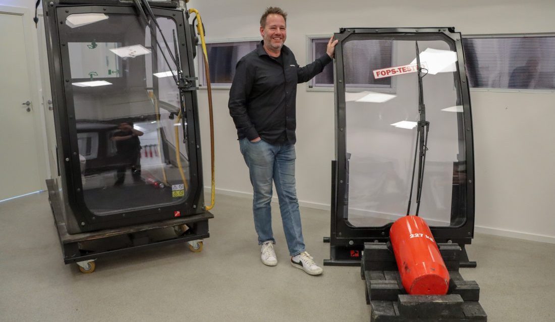 Florian Lauterbach, ansvarlig for Hammerglass Automotive, viser frem sikkerhetsglasset som oppfyller kravene til en rekke sikkerhetsstandarder, blant annet FOPS-nivå II. Sistnevnte test består i å slippe et 227 kilo tungt lodd fra 5,2 meters høyde ned på ruten, og ruten stopper loddet fra å trenge inn i førerhuset. (Foto: Njål Hagen)