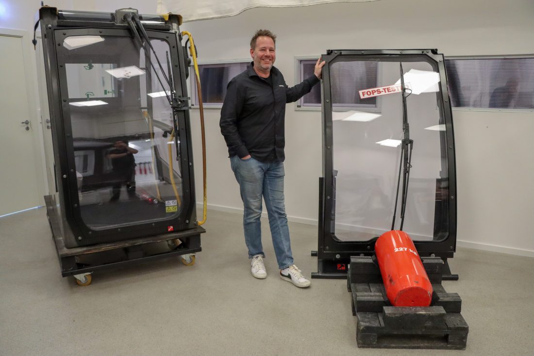 Florian Lauterbach, ansvarlig for Hammerglass Automotive, viser frem sikkerhetsglasset som oppfyller kravene til en rekke sikkerhetsstandarder, blant annet FOPS-nivå II. Sistnevnte test består i å slippe et 227 kilo tungt lodd fra 5,2 meters høyde ned på ruten, og ruten stopper loddet fra å trenge inn i førerhuset. (Foto: Njål Hagen)