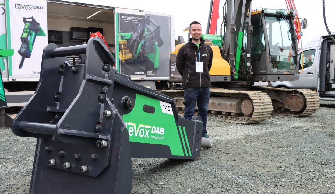 Per Joar Myhre, daglig leder i Levox, viser frem det helt nye produktet de har utviklet - skrapeplate for pigghammer. I bakgrunnen vises Acculinder-systemet påmontert en Volvo-graver. (Foto: Njål Hagen)