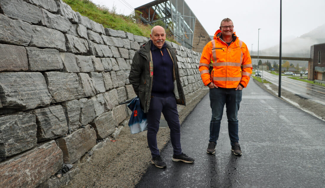 Jon Paul Grebstad, eier av Volda Maskin og som i dag jobber med prosjekt og kalkulasjon, og Erlend Lindset, anleggsleder i Volda Maskin, ved natursteinsmuren selskapet har murt opp langs gang- og sykkelveien fra Loen Skylift til Solvik. (Foto: Njål Hagen)